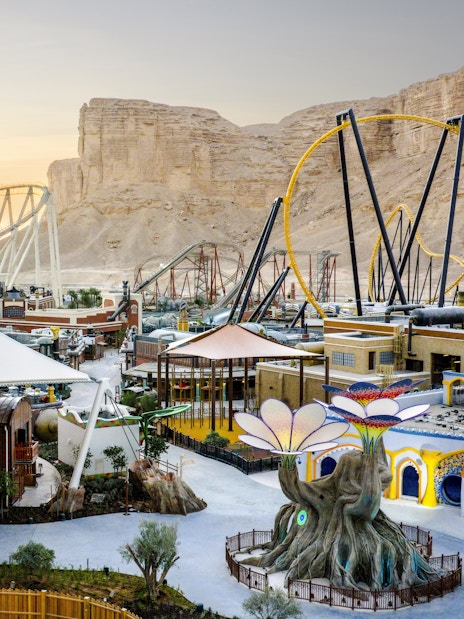 Aerial view of Six Flags Qiddiya with roller coasters and themed buildings against a desert backdrop.