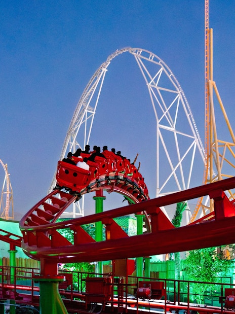 Roller coaster at Six Flags Qiddiya City with riders on a loop against a clear sky.