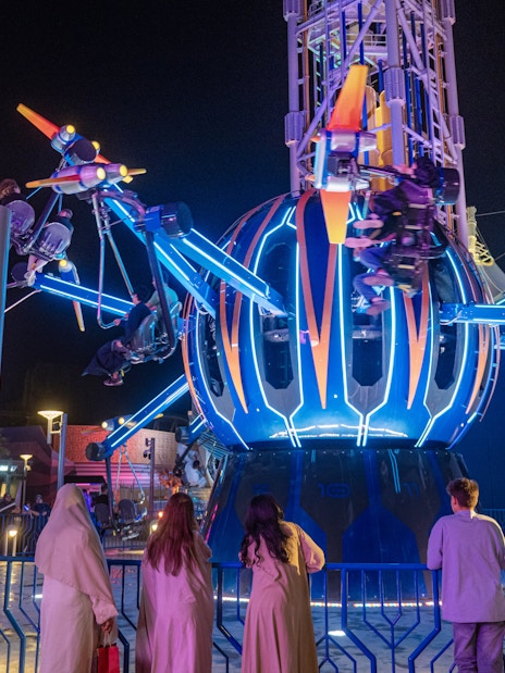 Thrill ride at night in Six Flags Qiddiya City with people enjoying the attraction.